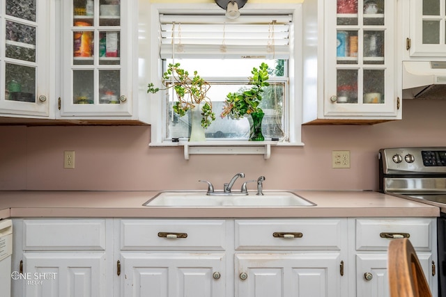 kitchen with glass insert cabinets, light countertops, a sink, and stainless steel range with electric cooktop