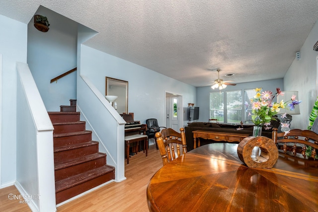 dining area with light wood-type flooring, ceiling fan, stairway, and a textured ceiling