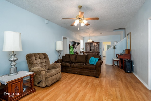 living area with light wood finished floors, stairway, ceiling fan, a textured ceiling, and baseboards