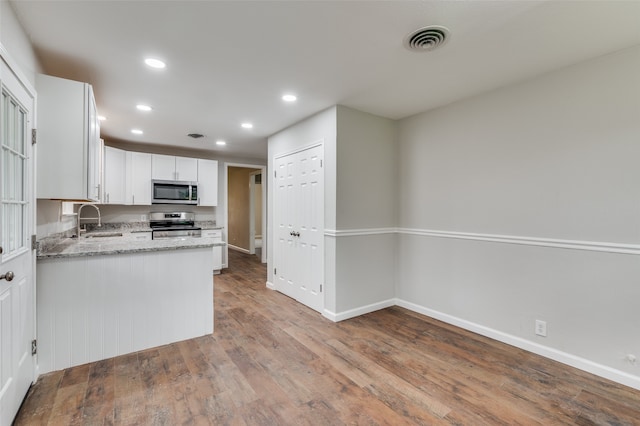 kitchen with appliances with stainless steel finishes, light stone counters, sink, hardwood / wood-style flooring, and white cabinets