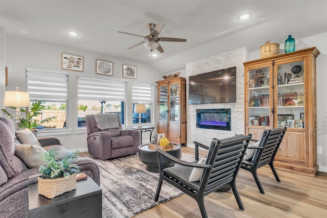 living room with ceiling fan, light hardwood / wood-style floors, a stone fireplace, and lofted ceiling