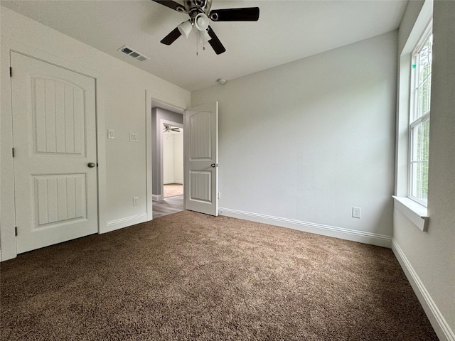 unfurnished bedroom with dark carpet, multiple windows, and ceiling fan