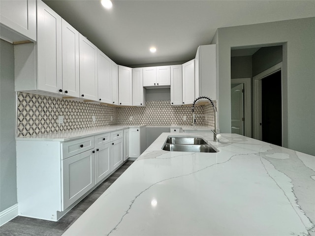 kitchen featuring decorative backsplash, light stone countertops, white cabinetry, and sink