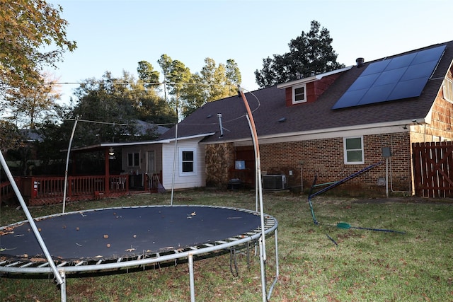 rear view of house featuring solar panels, a trampoline, central AC, and a lawn