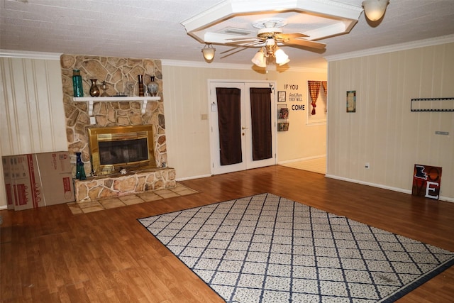 unfurnished living room with crown molding, ceiling fan, hardwood / wood-style floors, a stone fireplace, and french doors