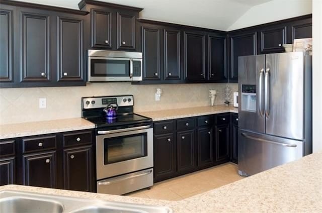 kitchen featuring appliances with stainless steel finishes, vaulted ceiling, decorative backsplash, and light tile patterned floors