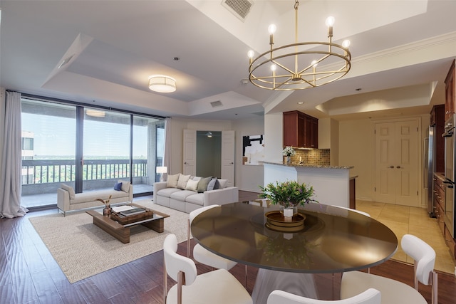 dining area featuring an inviting chandelier, expansive windows, a raised ceiling, and light hardwood / wood-style flooring