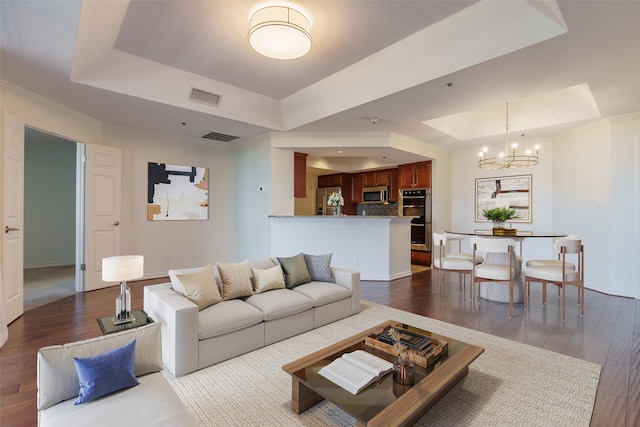 living room featuring a raised ceiling, an inviting chandelier, ornamental molding, and hardwood / wood-style flooring