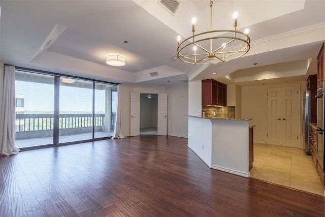 kitchen with a notable chandelier, wood-type flooring, backsplash, and a tray ceiling