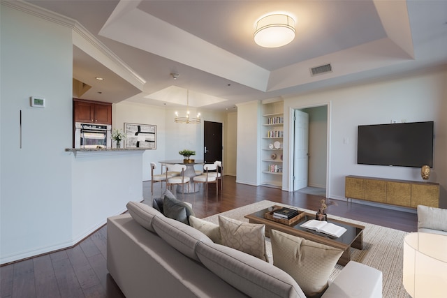 living room with dark hardwood / wood-style floors, a raised ceiling, built in features, and an inviting chandelier