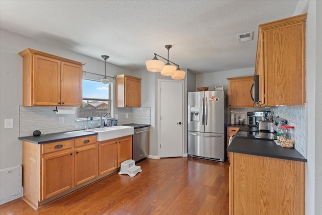 kitchen with appliances with stainless steel finishes, backsplash, decorative light fixtures, and dark hardwood / wood-style floors