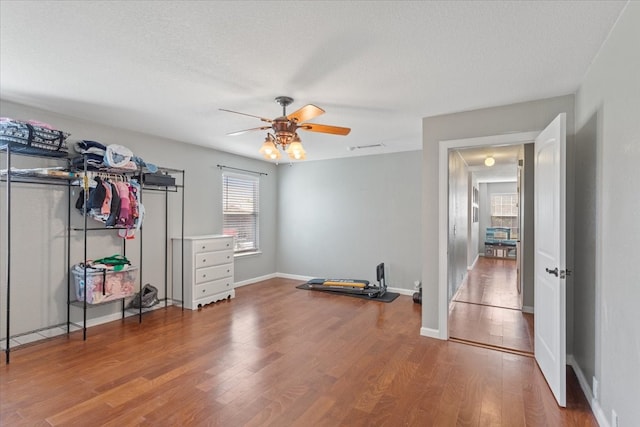 exercise area featuring ceiling fan, wood-type flooring, and a textured ceiling