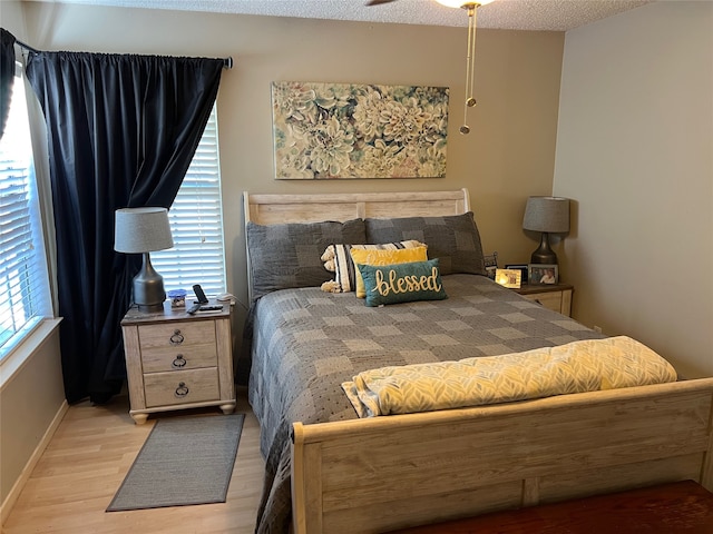 bedroom with a textured ceiling, light hardwood / wood-style floors, multiple windows, and ceiling fan