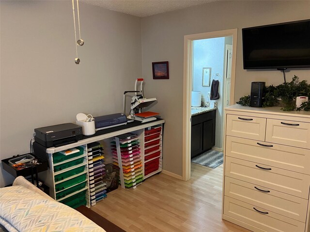 bedroom with a textured ceiling, connected bathroom, and light hardwood / wood-style flooring