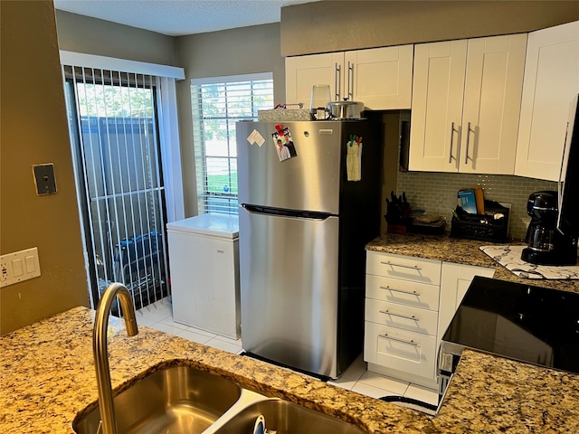 kitchen with sink, stone counters, white cabinets, stainless steel refrigerator, and black / electric stove