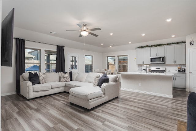 living room featuring light hardwood / wood-style floors, ceiling fan, and a healthy amount of sunlight