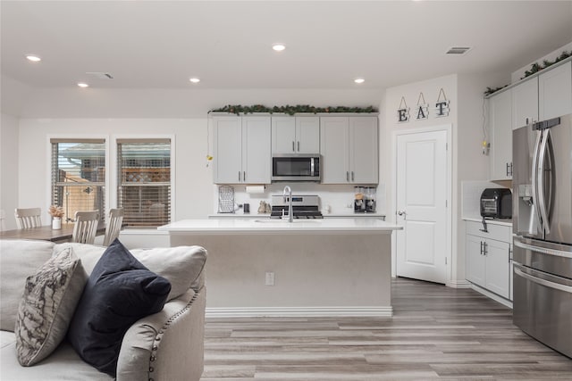 kitchen with white cabinetry, stainless steel appliances, a kitchen island with sink, and light hardwood / wood-style flooring