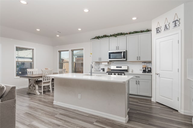 kitchen featuring tasteful backsplash, a kitchen island with sink, sink, hardwood / wood-style flooring, and white range with gas stovetop