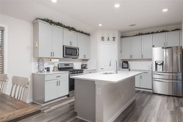 kitchen with appliances with stainless steel finishes, dark hardwood / wood-style flooring, a kitchen island with sink, sink, and white cabinetry