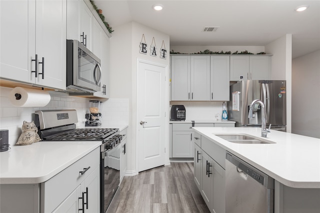 kitchen featuring backsplash, stainless steel appliances, sink, hardwood / wood-style flooring, and an island with sink