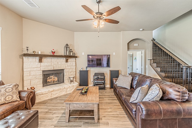 living room with ceiling fan, a stone fireplace, and light hardwood / wood-style flooring