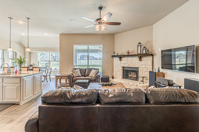 living room featuring light wood-type flooring, a textured ceiling, ceiling fan, sink, and a fireplace