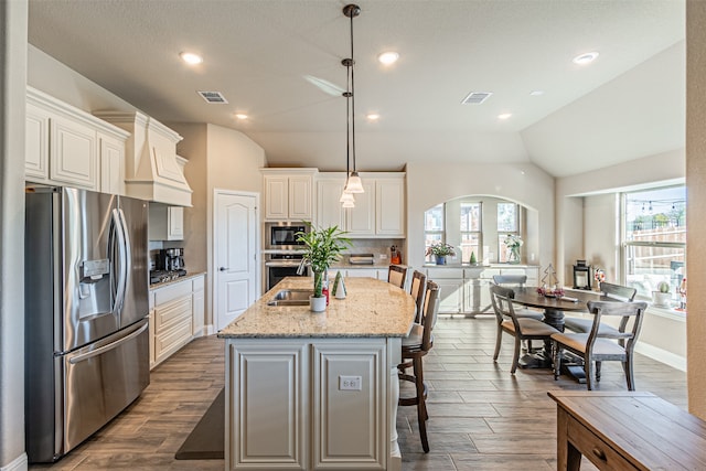 kitchen with light stone countertops, stainless steel appliances, an island with sink, pendant lighting, and vaulted ceiling