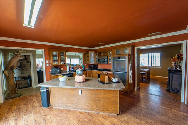 kitchen with hardwood / wood-style floors, stainless steel appliances, a kitchen island, and ornamental molding