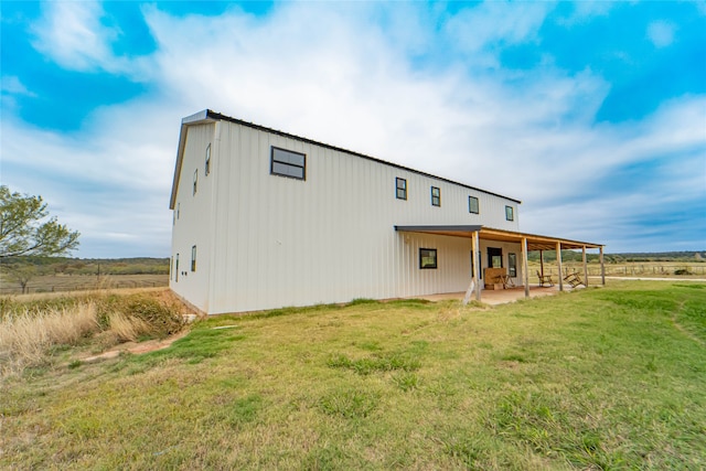 rear view of house featuring a patio, a rural view, and a lawn