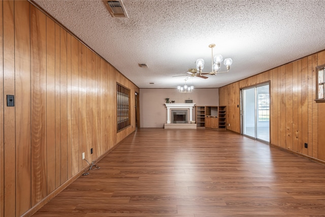 unfurnished living room featuring hardwood / wood-style floors, ceiling fan with notable chandelier, a textured ceiling, and wooden walls