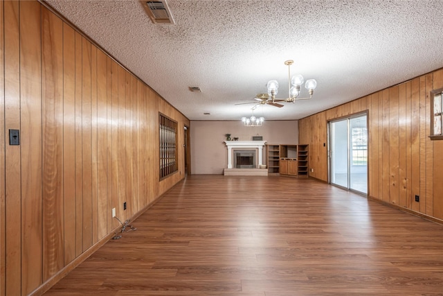 unfurnished living room with an inviting chandelier, wood-type flooring, wooden walls, and a textured ceiling