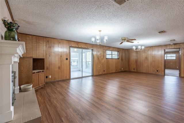 unfurnished living room with wooden walls, ceiling fan with notable chandelier, a textured ceiling, and hardwood / wood-style flooring