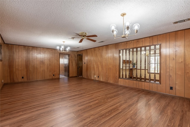 empty room with hardwood / wood-style flooring, ceiling fan with notable chandelier, wood walls, and a textured ceiling