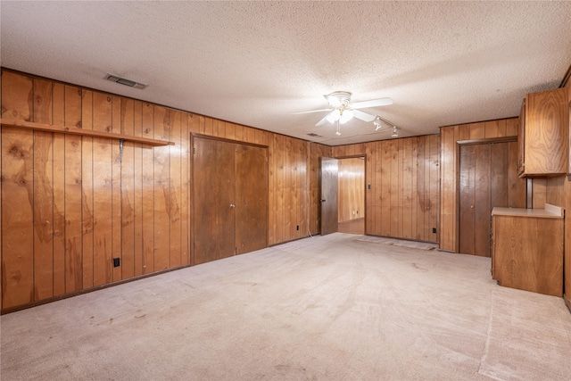 unfurnished room featuring light carpet, a textured ceiling, ceiling fan, and wooden walls