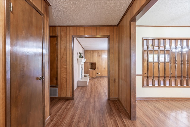 hall with hardwood / wood-style flooring, crown molding, a textured ceiling, and wooden walls