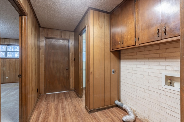 laundry room with hookup for an electric dryer, cabinets, a textured ceiling, light hardwood / wood-style flooring, and wood walls