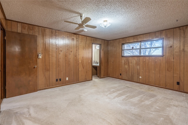 interior space featuring ceiling fan, light colored carpet, a textured ceiling, and wooden walls