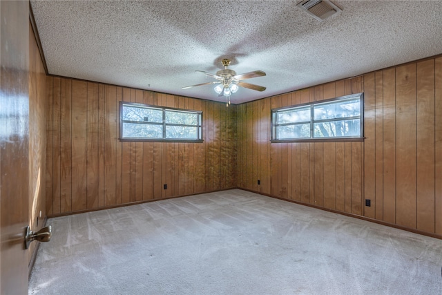 carpeted spare room featuring ceiling fan, wood walls, a textured ceiling, and a wealth of natural light