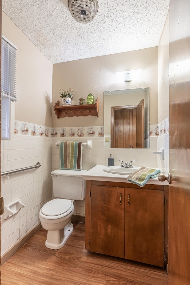 bathroom with vanity, a textured ceiling, hardwood / wood-style flooring, tile walls, and toilet