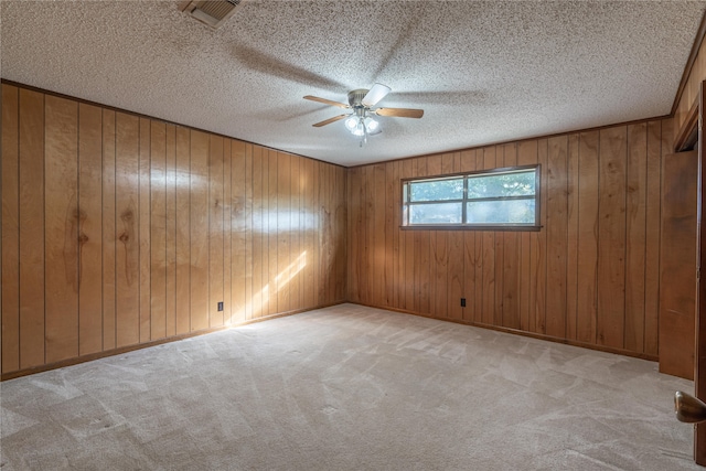 spare room featuring wood walls, ceiling fan, light carpet, and a textured ceiling