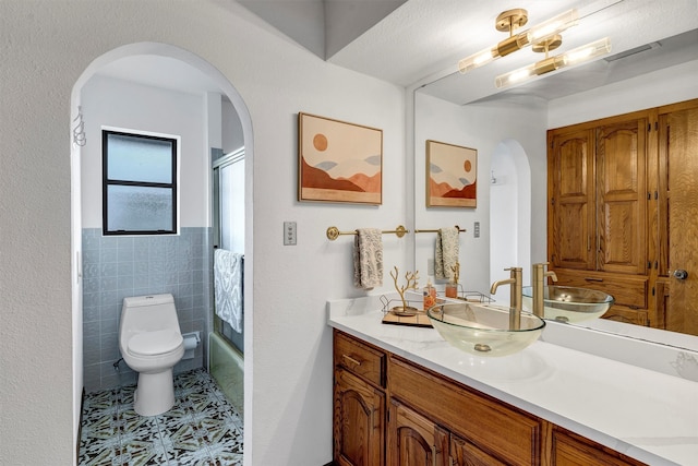 full bathroom with tile patterned floors, vanity, tile walls, enclosed tub / shower combo, and toilet