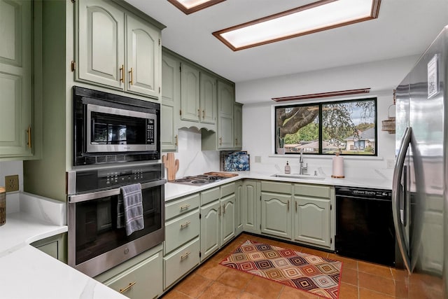 kitchen with sink, green cabinets, appliances with stainless steel finishes, dark tile patterned flooring, and decorative backsplash