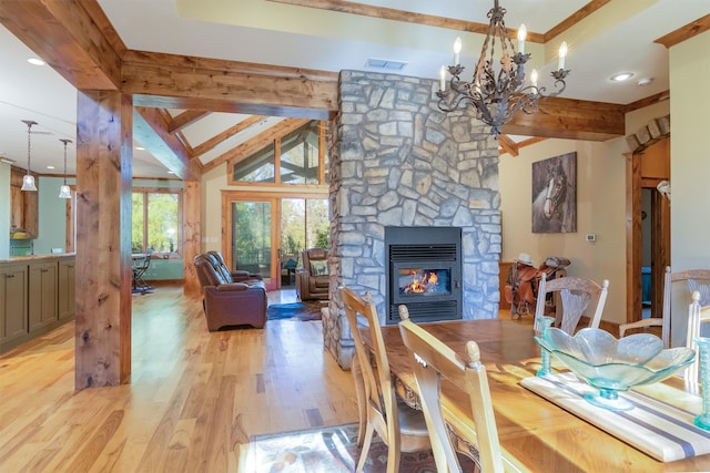 dining space featuring an inviting chandelier, a stone fireplace, light hardwood / wood-style flooring, and vaulted ceiling with beams