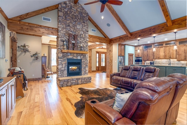 living room with a stone fireplace, a wealth of natural light, beam ceiling, and light wood-type flooring