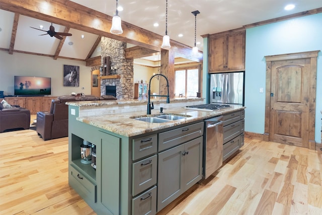 kitchen featuring appliances with stainless steel finishes, pendant lighting, an island with sink, sink, and light stone countertops