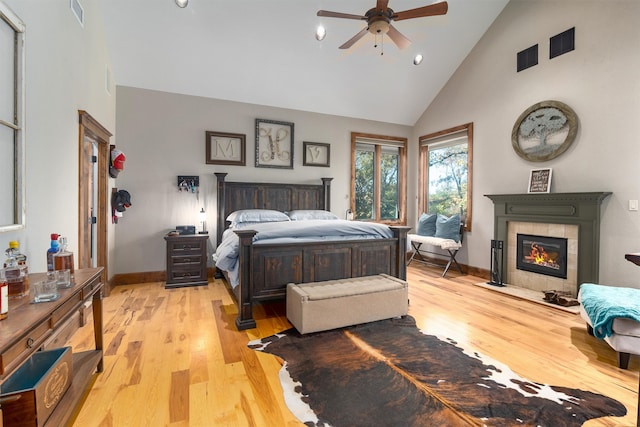 bedroom with a tiled fireplace, light hardwood / wood-style flooring, high vaulted ceiling, and ceiling fan