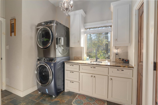 washroom with an inviting chandelier, stacked washer / drying machine, cabinets, and sink