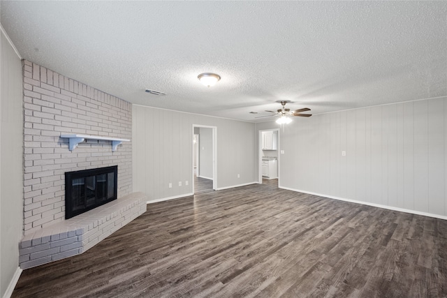 unfurnished living room featuring ceiling fan, dark hardwood / wood-style floors, a textured ceiling, wooden walls, and a fireplace