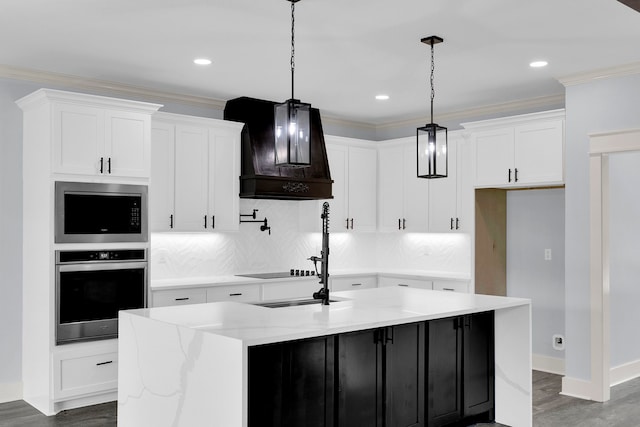 kitchen featuring appliances with stainless steel finishes, an island with sink, decorative light fixtures, white cabinets, and custom exhaust hood