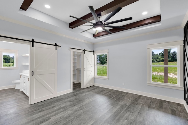 unfurnished bedroom featuring connected bathroom, ceiling fan, a barn door, a tray ceiling, and multiple windows